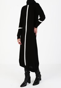 Robe en tricot noire à manches longues, ornée de rayures verticales blanches sur le devant et les manches. Une paire de bottes à talons hauts noires l'accompagne.