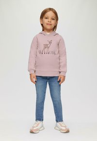 Roze sweatshirt met capuchon, voorzien van een hertgrafiek en de tekst "oh dear", gecombineerd met blauwe denim jeans en pastelkleurige sneakers.