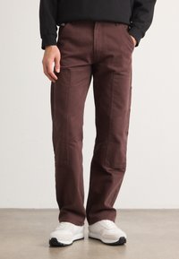 Pantaloni cargo bordeaux in tessuto di cotone, con tasche laterali e design a gamba dritta, abbinati a scarpe da ginnastica bianche.