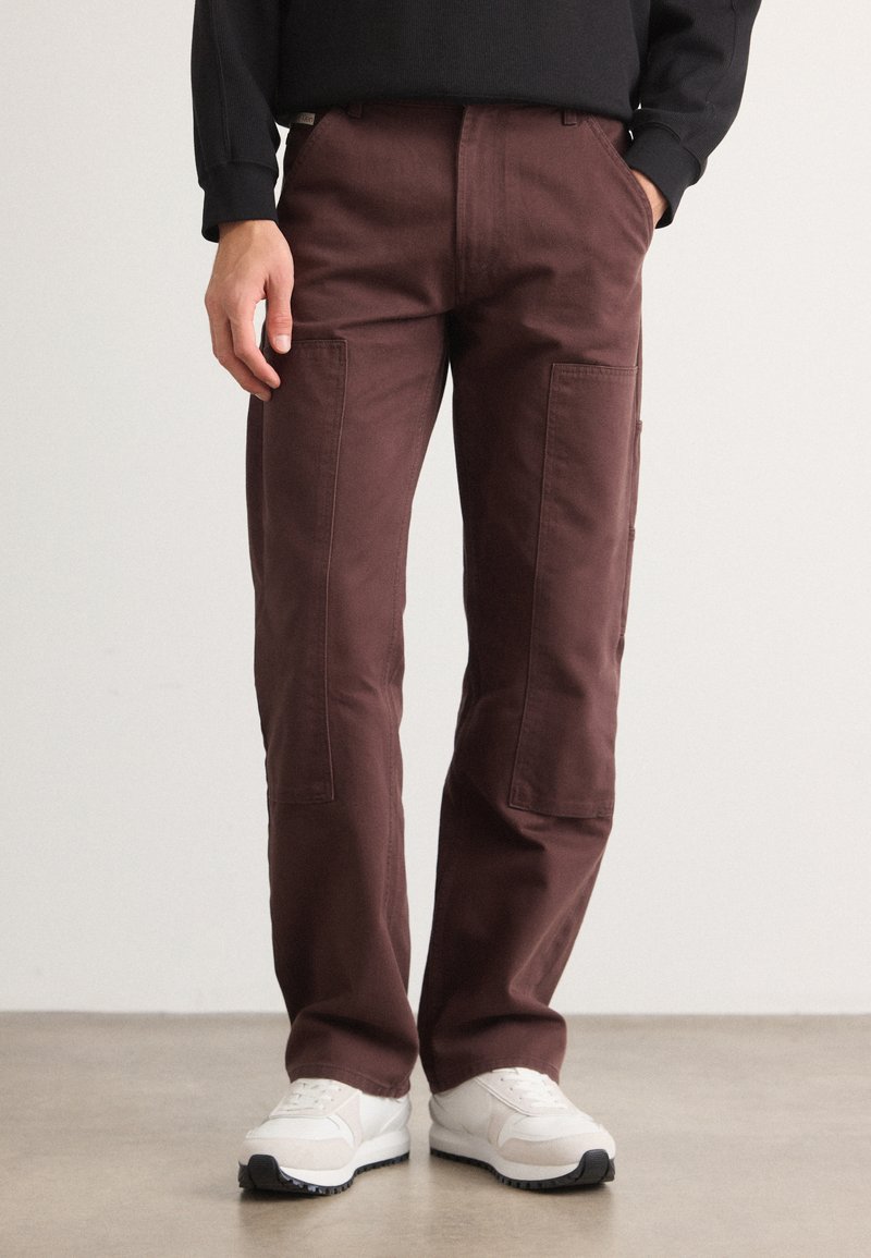 Pantaloni cargo bordeaux in tessuto di cotone, con tasche laterali e design a gamba dritta, abbinati a scarpe da ginnastica bianche.
