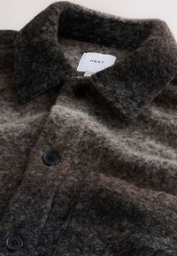 Giacca di lana marrone e grigia con bottoni neri, colletto e tasca sul petto, con etichetta "NEXT" all'interno del collo.