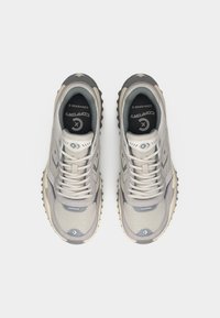 Ζευγάρι γκρι και μπεζ αθλητικά παπούτσια Converse με λογότυπα αστέρι, πλέγμα επάνω μέρος και ανθεκτικές σόλες, φαίνονται από πάνω σε λευκό φόντο.