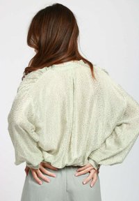 Blusa verde chiaro con tessuto leggero e texture, maniche ampie, orlo arricciato e scollatura rotonda. Presenta un delicato motivo a pois.