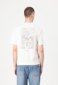 Balta T-kreklā ar īsām piedurknēm, aizmugurē ir melns līniju mākslas grafiks, attēlojot arhitektoniskus elementus un dabas detaļas. Ikdienišķa piegriezuma.