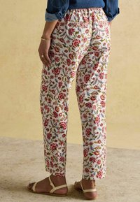 Białe spodnie w kwiatowy wzór z czerwonymi, zielonymi i niebieskimi wzorami; miękki materiał; elastyczna talia; prosty krój nogawek; noszone z płaskimi sandałami.