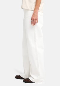 Λευκό τζιν παντελόνι με φαρδύ πόδι και ξεφτισμένη λεπτομέρεια στο τελείωμα. Κατασκευασμένο από παχύ ύφασμα, με αντίθετες ραφές και κλασικό σχέδιο με πέντε τσέπες.