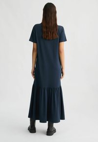 Abito lungo blu navy realizzato in tessuto morbido, con scollatura rotonda, maniche corte e orlo arricciato. Stivali alla caviglia neri.