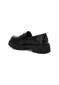 Zapatos de piel negra tipo slip-on con una suela de goma gruesa, que presentan una textura suave y una correa ancha en la parte superior.