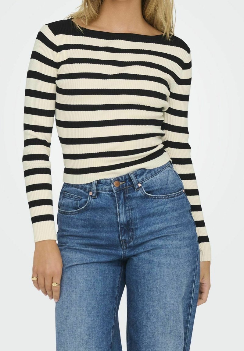 Personne portant un haut à manches longues rayé noir et blanc, rentré dans un jean denim bleu taille haute avec poches avant.