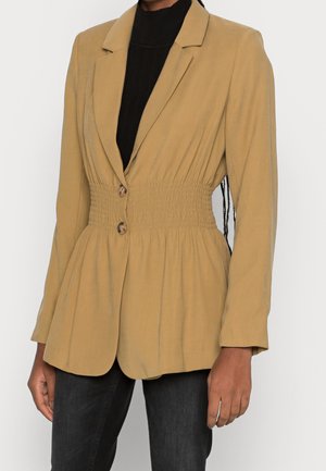 Mustard yellow blazer with a fitted waist, smock detailing, and two front buttons; smooth fabric, long sleeves, and notched collar.