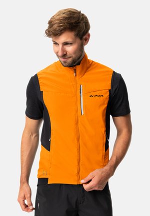 Leichte orangefarbene Weste mit hohem Kragen, Reißverschluss, Seitentaschen und kontrastierendem schwarzen Stoff an den Schultern. Logo auf der Brust aufgedruckt.