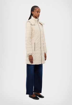 Veste matelassée beige avec un col montant, fermeture éclair frontale et deux poches latérales ; comprend une capuche amovible et un subtil détail de couture.
