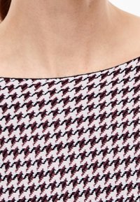 Top en maille avec un motif pied-de-poule noir, bordeaux et blanc. Encolure arrondie et texture lisse. Vue rapprochée du tissu.