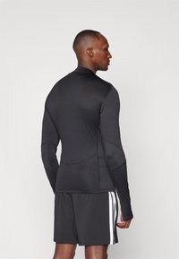 Schwarzes langärmliges Sportshirt mit enganliegendem Design, strukturiertem Stoff und flachen Nähten, kombiniert mit schwarzen Shorts mit weißen Streifen.