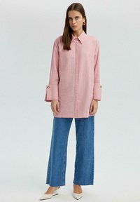 Chemise à rayures roses avec un col et de larges poignets. Associée à un jean large bleu clair et des chaussures blanches à bout pointu.