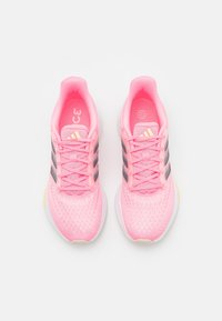 Vaaleanpunaiset urheilukengät, joissa on verkkokangasyläosa, kolmea mustaa raitaakselia, teksturoituja yksityiskohtia ja pehmustettu pohja keltaisilla korostuksilla.