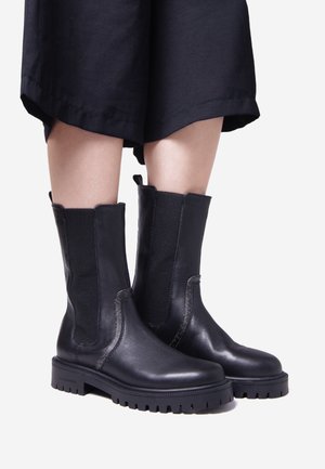 Black leather ankle boots with elastic side panels, textured finish, and rugged rubber sole. Features stitching accents and pull tabs.