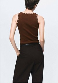 Top brown fără mâneci cu ținte argintii pe cusăturile umerilor, asortat cu pantaloni negri cu talie înaltă. Material tricotat neted.