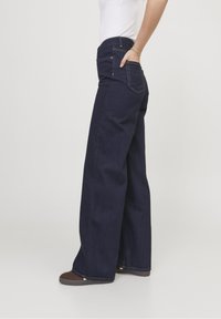 Široké tmavomodré džíny s vysokým pasem, jemnými detaily prošití a předními i zadními kapsami. Navrženy pro pohodlný střih.