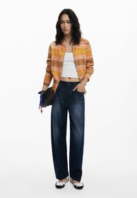 Överdimensionerad orange randig bomberjacka över en vit crop top, kombinerad med vida mörkblå jeans och svartvita slip-on skor.