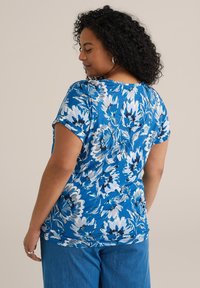 Kortärmad, blå blus med blommor som har vita och mörkblå blommor. Gjord av mjukt tyg med avslappnad passform och rundad halsringning.