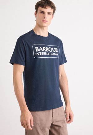 T-shirt de algodão azul-marinho com um logo retangular branco "BARBOUR INTERNATIONAL" na parte da frente, com um formato clássico de gola redonda e mangas curtas.