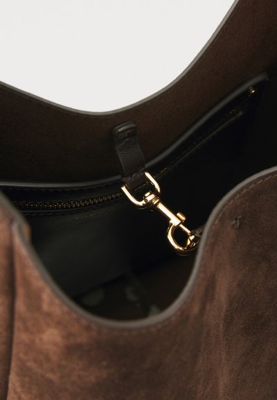 Intérieur d'un sac tote en suède marron avec un clip en métal doré et une poche zippée, mettant en valeur une texture lisse et une forme arrondie.