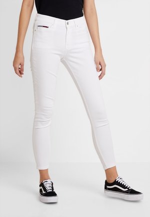 Vaqueros blancos ajustados de tiro alto, con diseño de cinco bolsillos y costuras en contraste, combinados con deportivas negras de corte bajo.