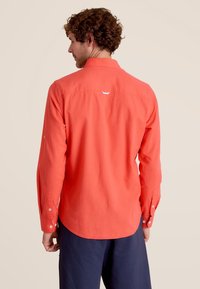 Chemise à manches longues pour homme en corail vif, fabriquée dans un tissu texturé. Dispose de poignets à boutons et d'un petit détail en boucle à l'arrière.