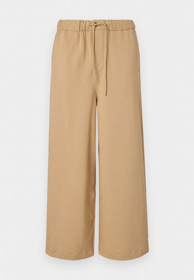 Beige laiad püksid, mis on valmistatud pehmest kangast, elastse vöökohtiga ja nööriga, küljetaskudega ja sirge lõikega.