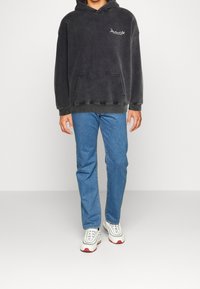 Donkergrijze oversized hoodie met een voorzak en een wit logo, gecombineerd met blauwe recht gesneden jeans en sneakers met rode accenten.