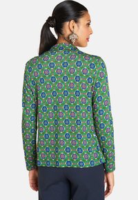Green patterned jacket with a floral design in blue and red, featuring long sleeves and a collar. The fabric has a textured appearance.