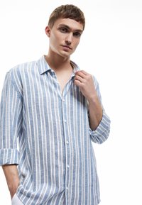 Kuvitettu paita, jossa on sinivalkoiset pystysuorat raidat. Kevyestä kankaasta valmistettu, siinä on kaulus ja käärityt hihat.