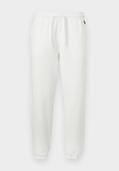 Λευκά παντελόνια φόρμας από φλις με ελαστική μέση, κορδόνια, ελαστικές μανσέτες και μικρό μαύρο λογότυπο κοντά στο ισχίο σε μονόχρωμο φόντο.