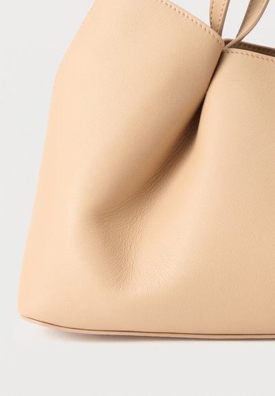 Μαλακό μπεζ δερμάτινο τσάντα χειρός με εμφανείς ραφές και ελαφρώς τσαλακωμένη υφή σε απλό λευκό φόντο.