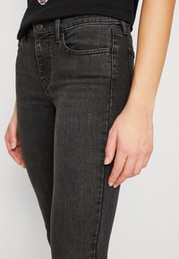 Vaqueros skinny de mezclilla negra con un clásico diseño de cinco bolsillos, cierre frontal con botón y sutiles detalles de costura en los bolsillos.