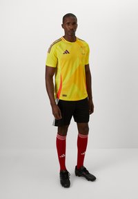Gul fodboldtrøje med røde og lilla accenter, sorte shorts, røde sokker med hvide striber og sorte støvler; designet til atletisk tøj.