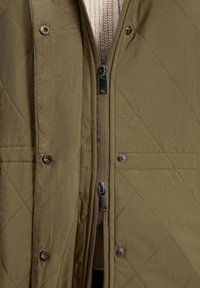 Olivi vihreä tikattu liivi, jossa on vetoketju ja näppärät nepparit. Liivissä on sileä, kevyt kangas ja ribbikuvioitu sisätekstuuri.