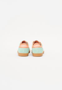 Green suede sneakers with orange accents at the heel, rubber sole, and white logo on the back. Smooth texture with a low-top design.