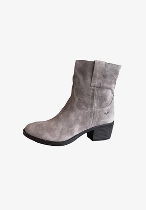 Grijze suède enkellaars met een lage gestapelde hak, een trekband en decoratieve stiksels aan de zijkant.