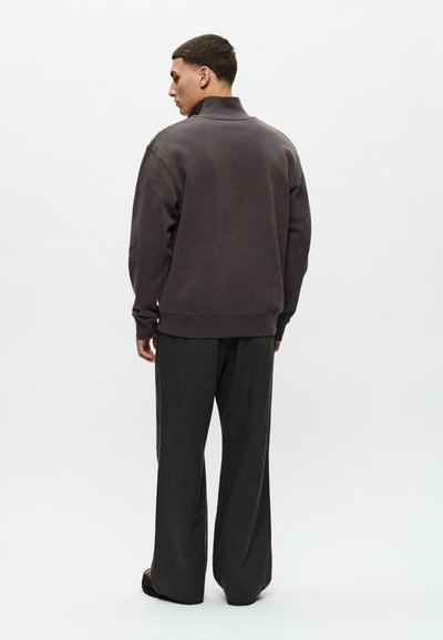 Sivý, ťažký bavlnený sweatshirt s vysokým golierom a dlhými rukávmi, spárovaný s voľnými šedými nohavicami. Žiadne viditeľné vzory ani kovové prvky.