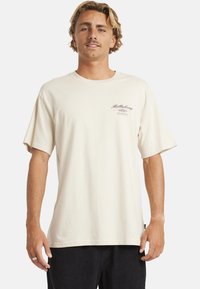 Crème-kleurig shirt met korte mouwen van katoen, met een klein grafisch logo op de linkerkant van de borst. Relaxte pasvorm met een ronde hals.