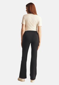 Pantalones acampanados negros con una textura suave, cintura alta y detalles de costura sutiles, combinados con una camiseta ajustada de color claro.