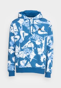 Modrá mikina s kapucí s texturovaným povrchem, zdobená bílým abstraktním potiskem loga Nike. Nastavitelná kapuce a detail přední kapsy. Žebrované manžety.