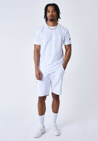 Conjunto atlético blanco que incluye una camiseta de manga corta y pantalones cortos, confeccionado en una tela suave, con detalles de logotipos sutiles y un corte relajado.
