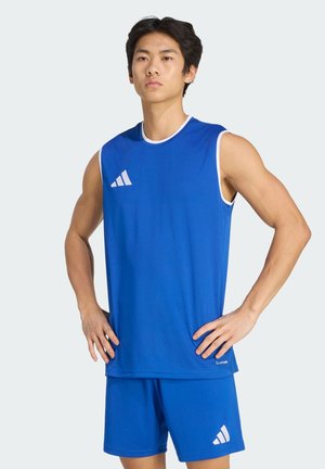 Jeune homme debout, les mains sur les hanches, portant un haut de sport bleu sans manches et un short assorti avec le logo blanc Adidas.