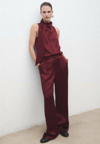 Bordeaux satijnen outfit met een hoge kraag top en broek met brede pijpen. Kenmerkt zich door een gladde textuur, een ontspannen pasvorm en zijzakken.