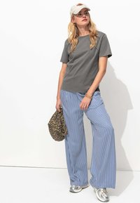 T-shirt gris à manches courtes associé à un pantalon large rayé bleu et blanc. Accessoirisé avec un sac à imprimé léopard et des baskets argentées.