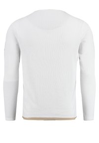 Chemise à manches longues blanche côtelée avec un col rond, présentant un tissu texturé et un petit accent beige à l'ourlet.