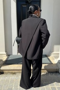 Melna, liela izmēra bleizeris ar pielāgotu piegriezumu, kombinēts ar platām melnām biksēm. Gluda auduma, valkāts ar mazu melnu somiņu un saules brillēm.